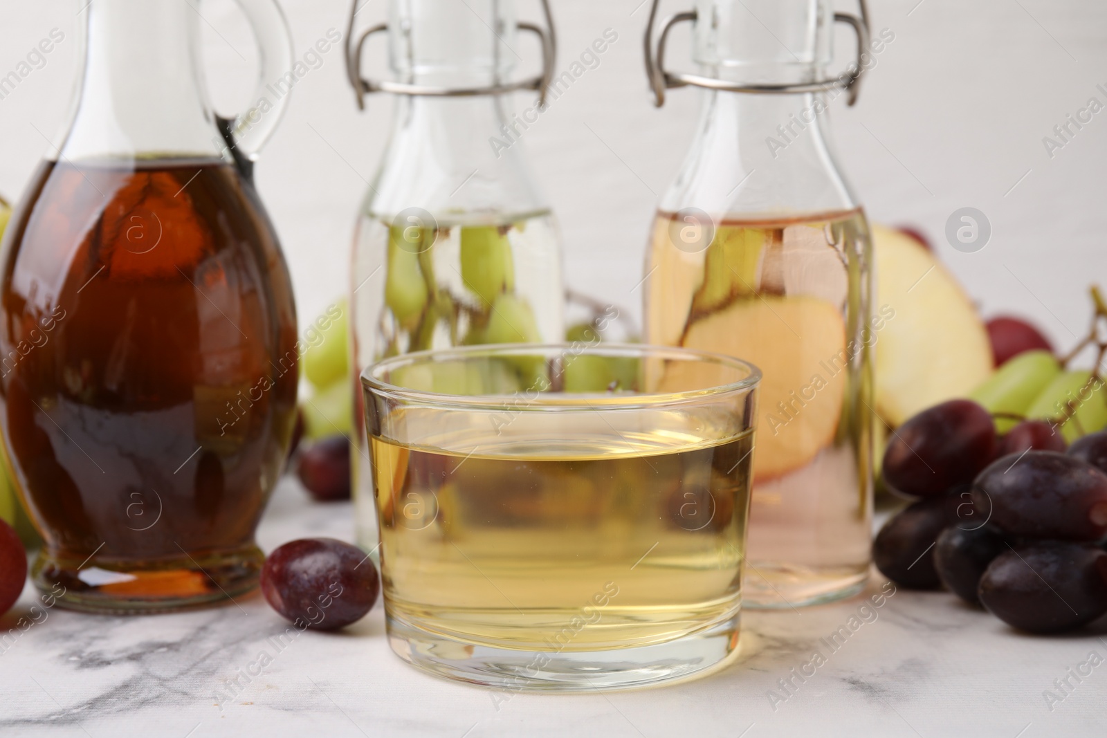 Photo of Different types of vinegar and grapes on light marble table, closeup