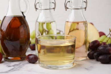 Photo of Different types of vinegar and grapes on light marble table, closeup