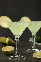 Delicious Margarita cocktail in glasses and limes on grey table