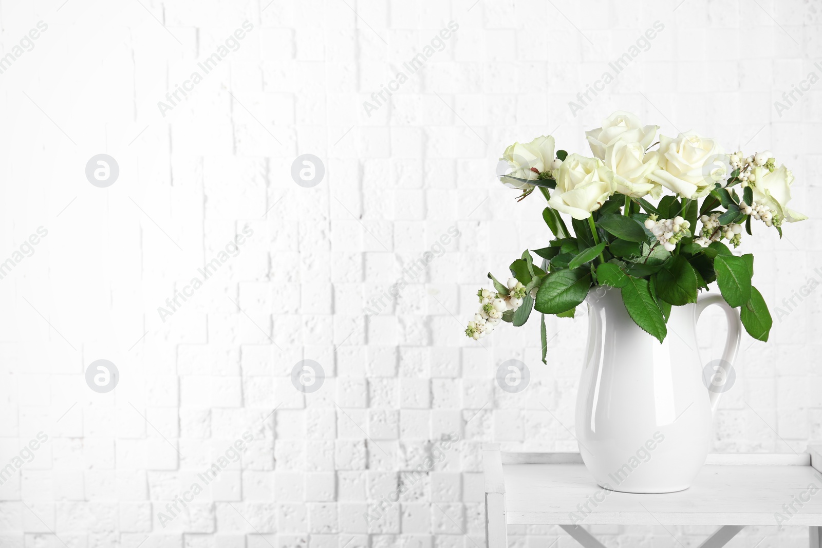 Photo of Vase with bouquet of beautiful flowers on table near brick wall. Space for text