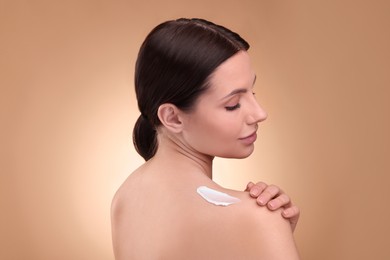 Photo of Beautiful woman with smear of body cream on her shoulder against light brown background