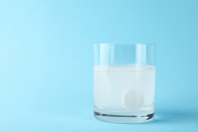 Glass of water with effervescent tablet on light blue background, space for text