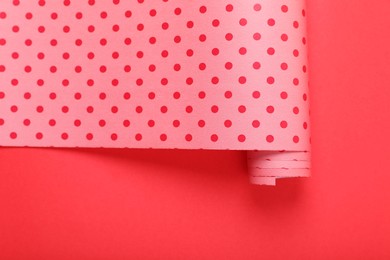 Photo of Roll of polka dot wrapping paper on red background, top view