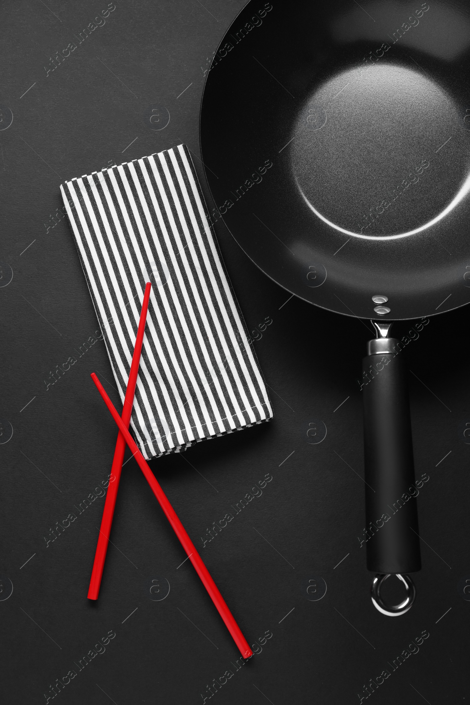 Photo of Empty iron wok and chopsticks on black table, flat lay