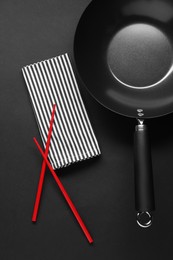 Empty iron wok and chopsticks on black table, flat lay