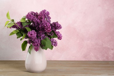 Photo of Beautiful lilac flowers in vase on wooden table, space for text