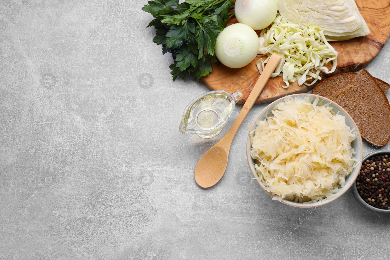 Photo of Bowl of tasty sauerkraut and ingredients on grey table, flat lay. Space for text