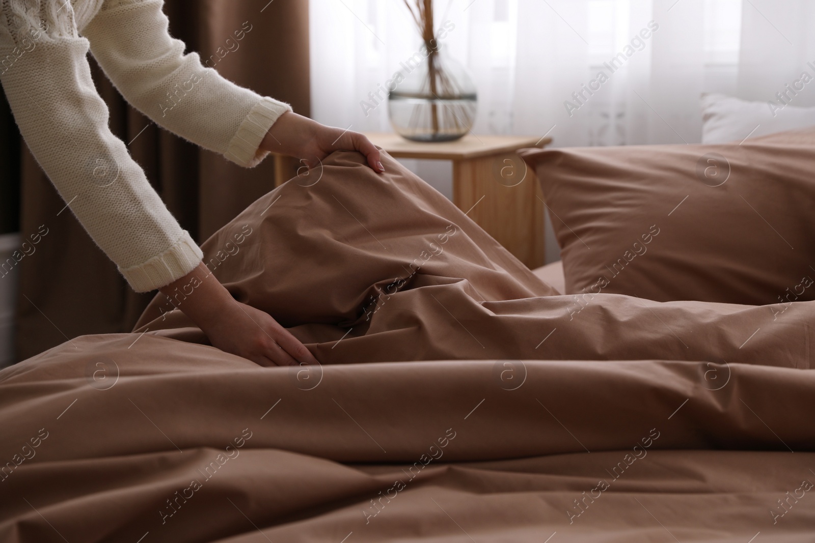 Photo of Woman making bed with brown linens, closeup