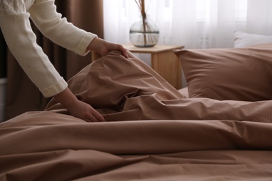 Woman making bed with brown linens, closeup