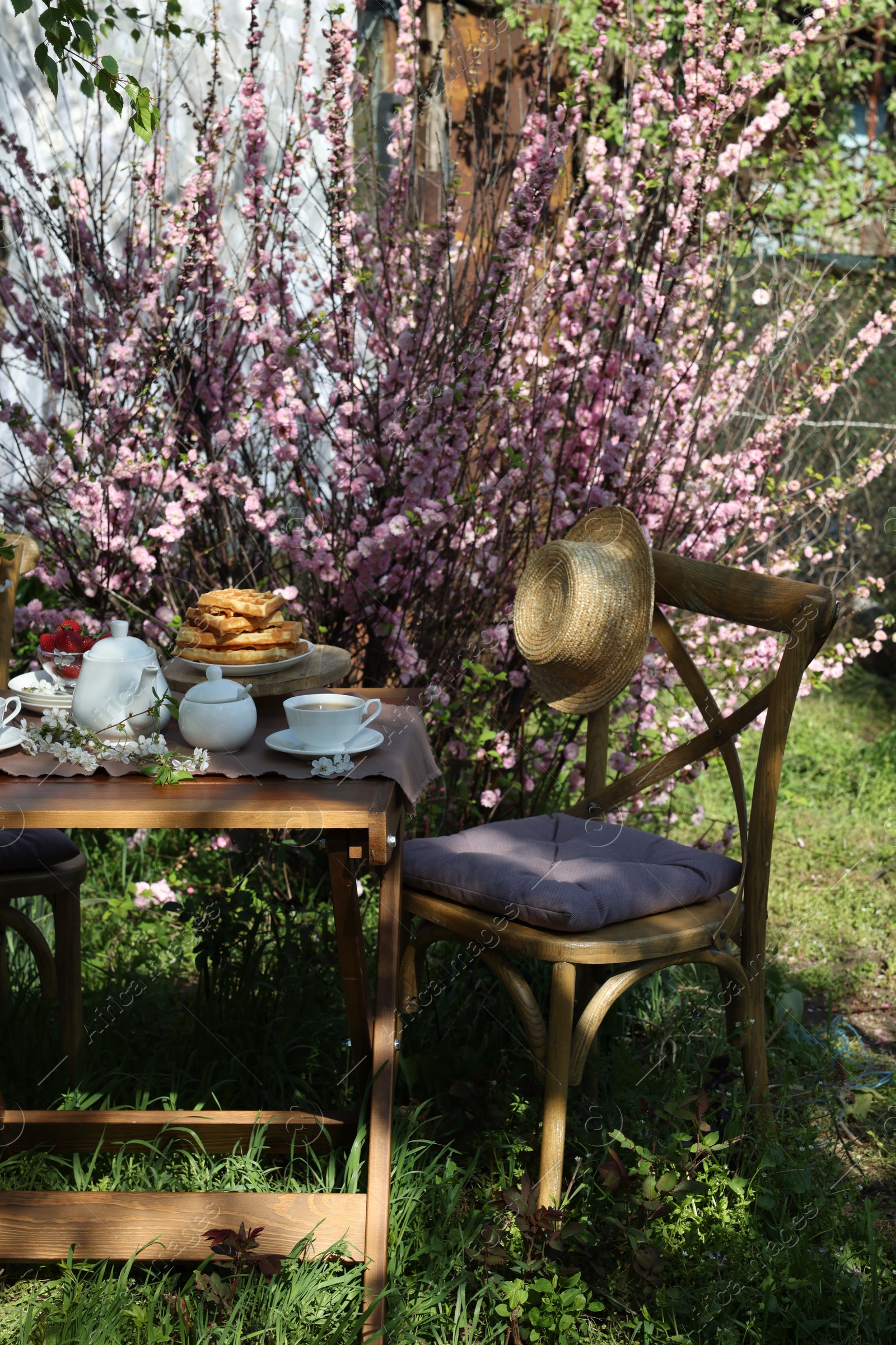 Photo of Beautiful spring flowers, freshly baked waffles and ripe strawberries on table served for tea drinking in garden