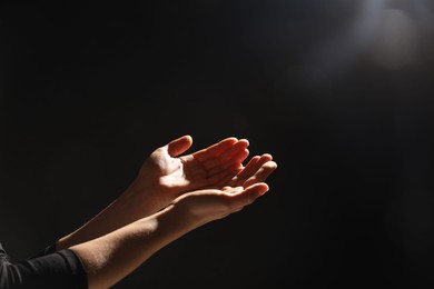 Photo of Religion. Woman with open palms praying on black background, closeup. Space for text