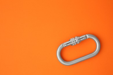 One metal carabiner on orange background, top view. Space for text