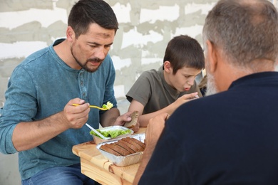 Poor people eating food at wooden table outdoors