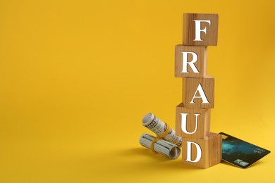 Photo of Wooden cubes with word Fraud, credit card and money on yellow background, space for text