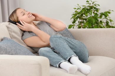 Teenage girl listening to music with headphones on sofa at home