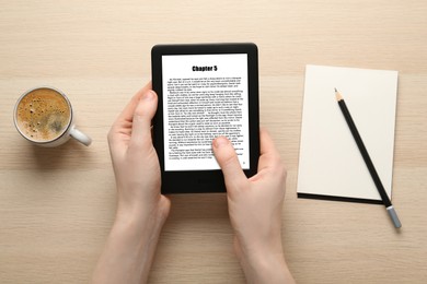 Image of Woman using e-book reader at wooden table, top view