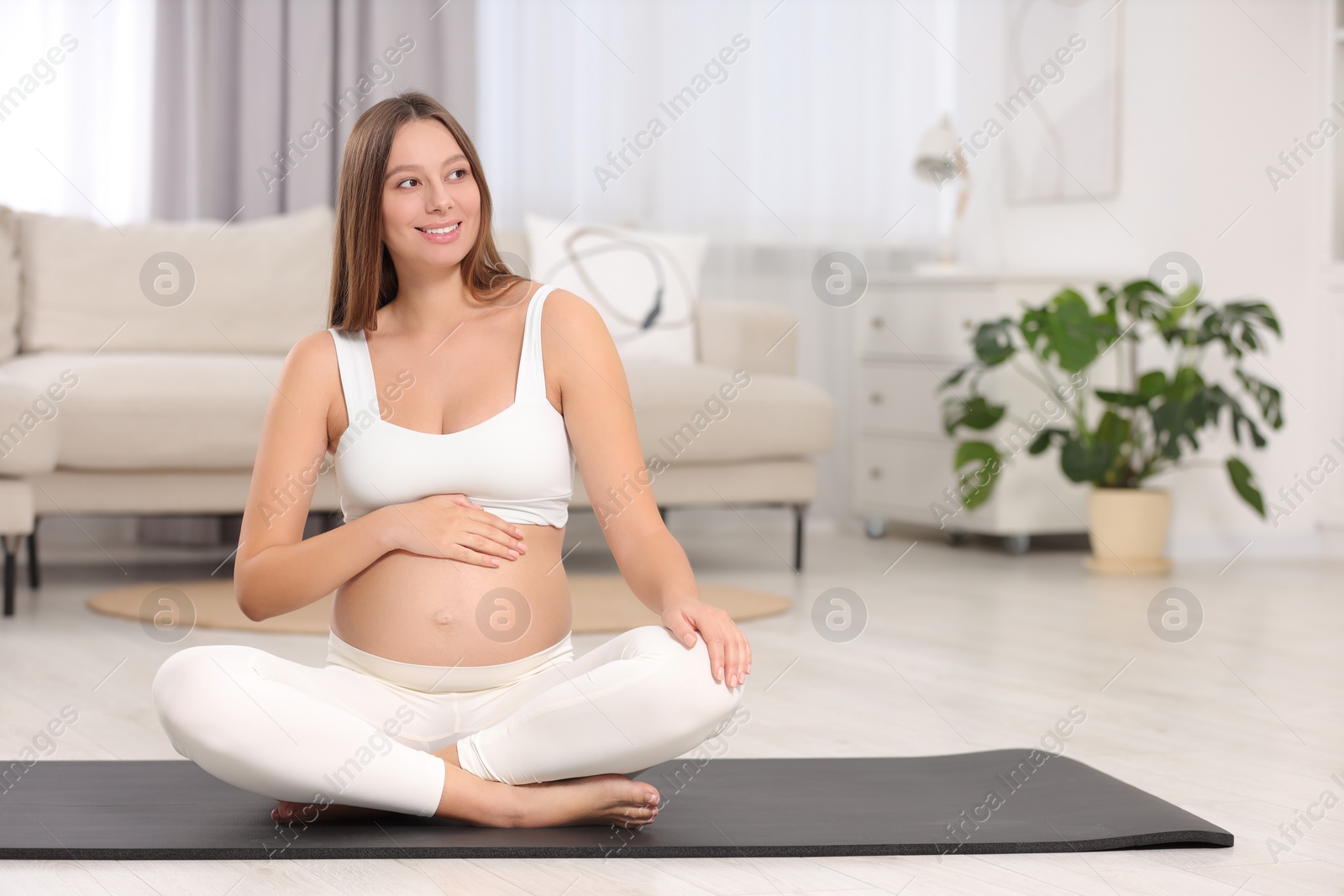 Photo of Beautiful pregnant woman sitting on yoga mat at home, space for text