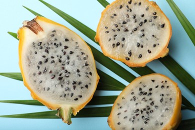 Delicious cut dragon fruits (pitahaya) and tropical leaf on light blue background, flat lay