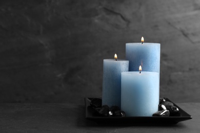 Photo of Dark plate with three burning candles and rocks on table, space for text