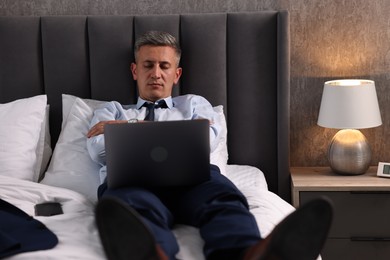 Businessman with laptop sleeping on bed indoors