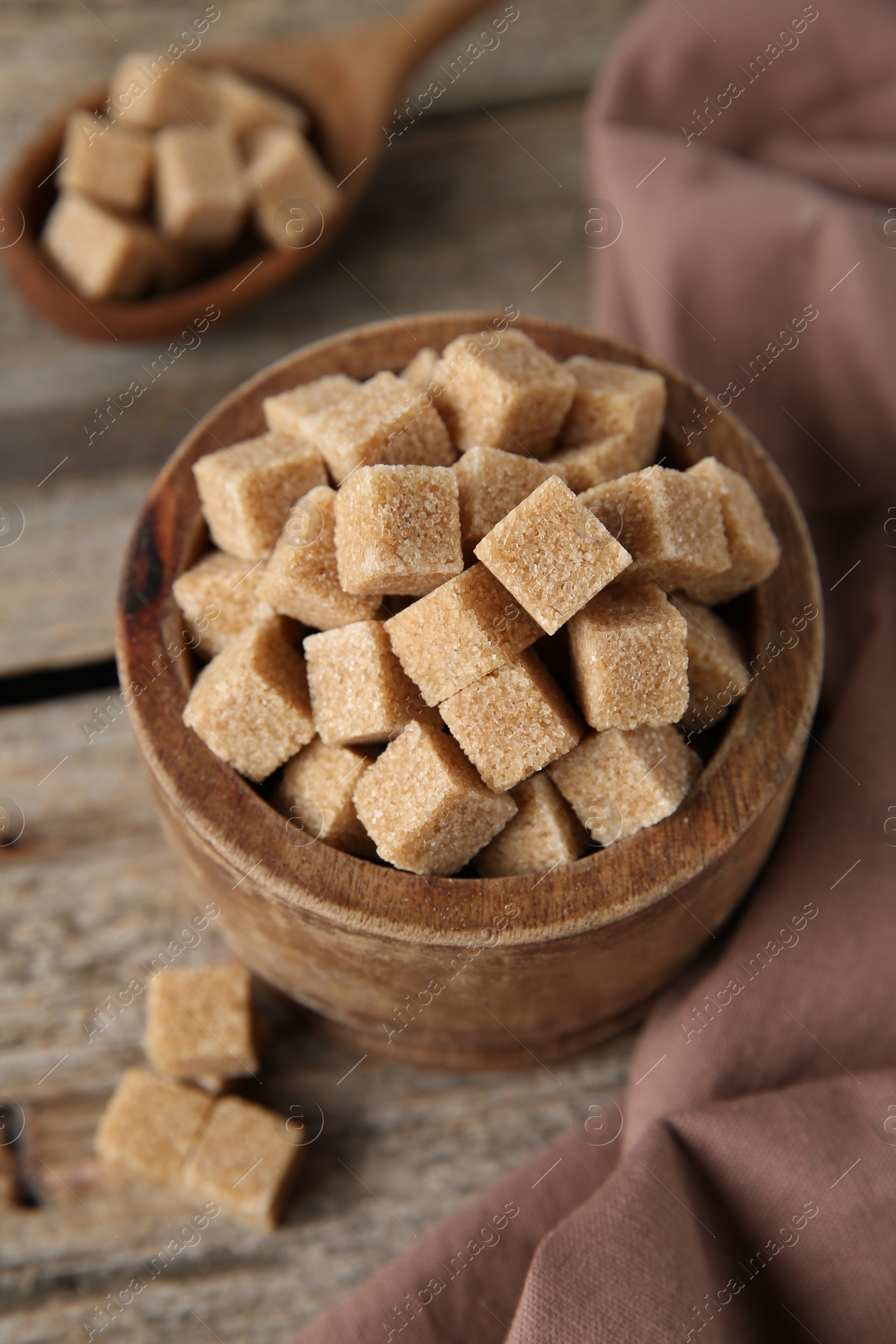 Photo of Brown sugar cubes in bowl on wooden table, closeup