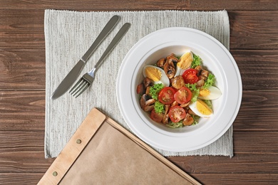 Photo of Plate with delicious fresh salad and menu on table, top view