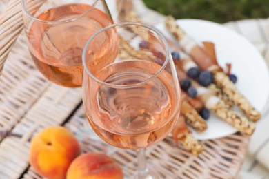 Glasses of delicious rose wine and food on picnic basket outdoors