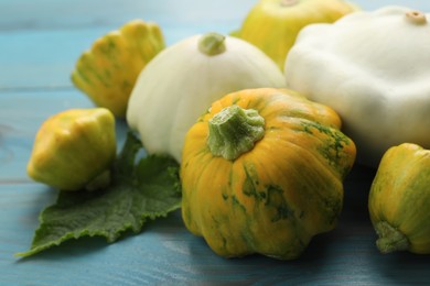 Photo of Fresh ripe pattypan squashes with leaf on light blue wooden table, closeup