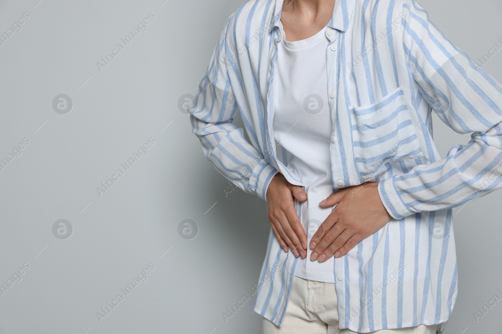 Photo of Young woman suffering from menstrual pain on light grey background, closeup. Space for text