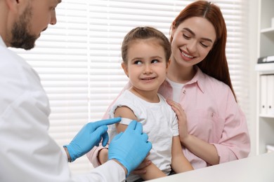 Children's hepatitis vaccination. Mother with her daughter in clinic. Doctor sticking medical plaster on little girl's arm