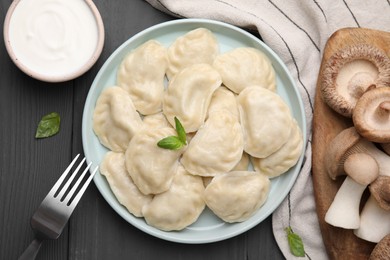 Photo of Plate of delicious dumplings (varenyky) with mushrooms on grey wooden table, flat lay