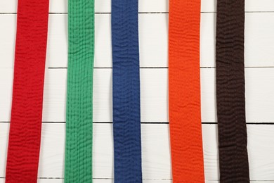 Photo of Colorful karate belts on wooden background, flat lay