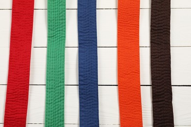 Colorful karate belts on wooden background, flat lay