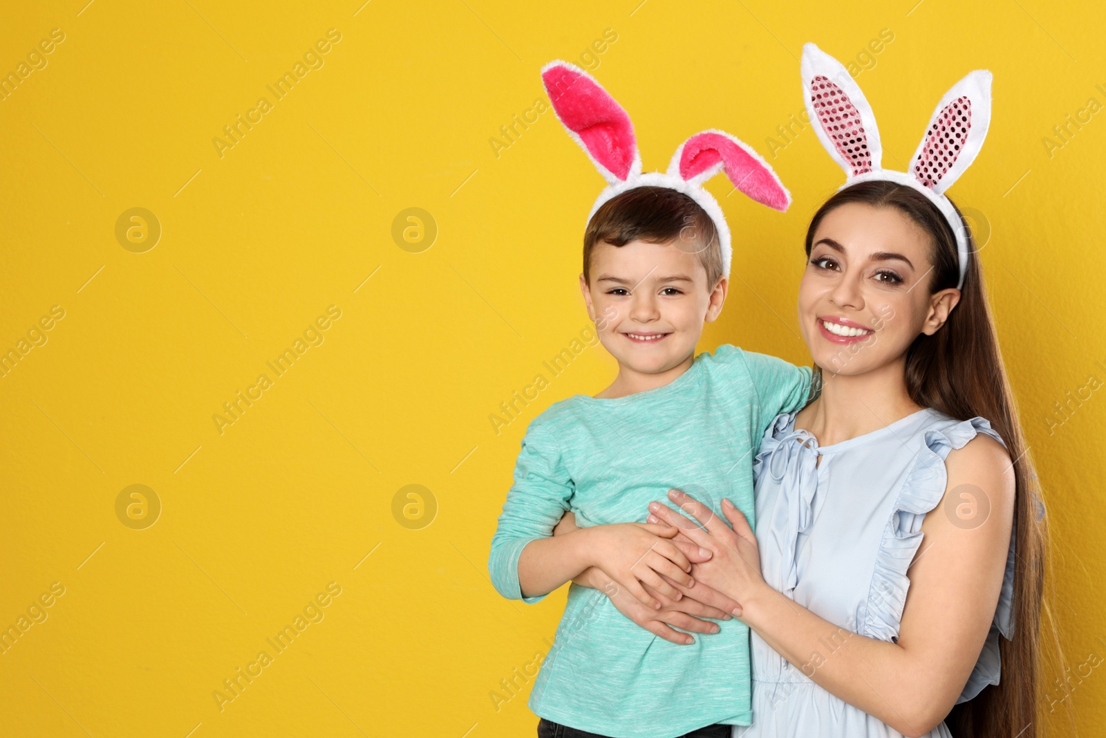 Photo of Mother and son in Easter bunny ears headbands on color background, space for text