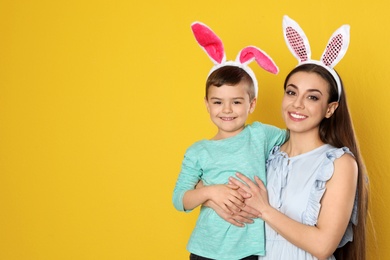 Mother and son in Easter bunny ears headbands on color background, space for text