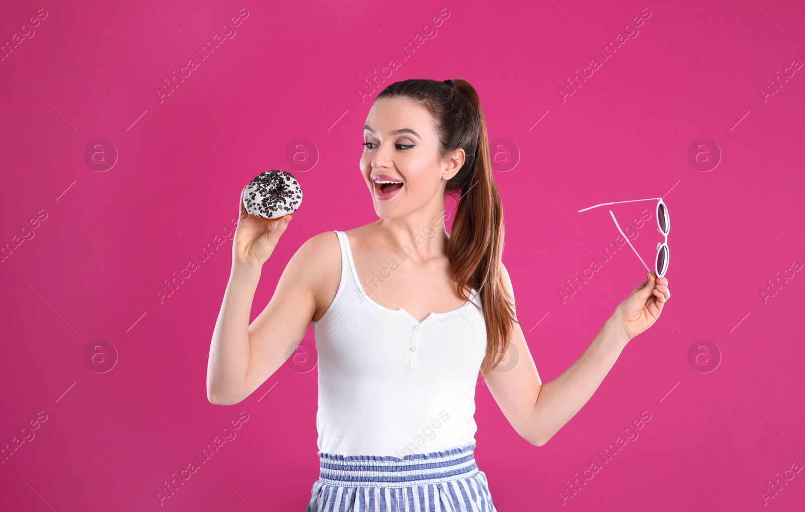 Photo of Beautiful young woman with donut and sunglasses on pink background