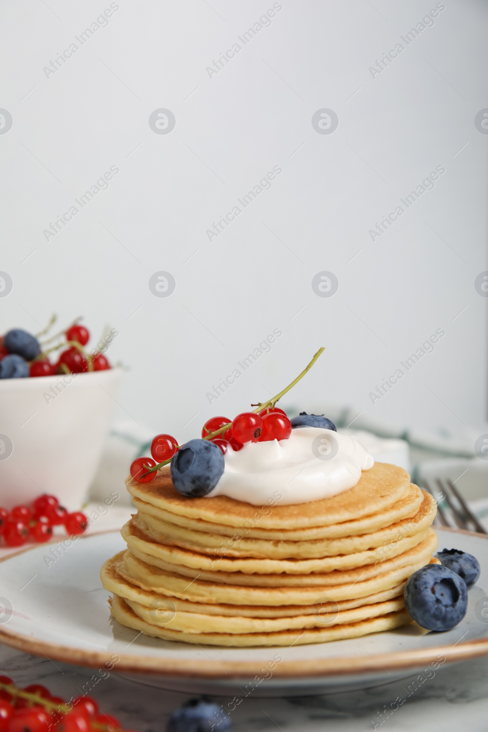 Photo of Tasty pancakes with natural yogurt, blueberries and red currants on marble table