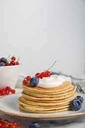 Photo of Tasty pancakes with natural yogurt, blueberries and red currants on marble table