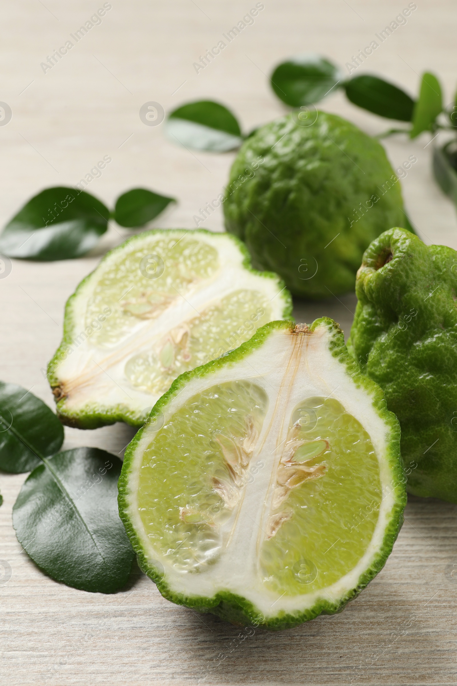 Photo of Whole and cut ripe bergamot fruits with green leaves on white wooden table, closeup