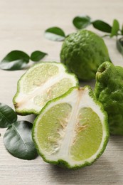 Whole and cut ripe bergamot fruits with green leaves on white wooden table, closeup