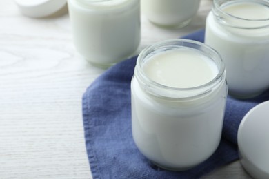 Photo of Tasty yogurt in glass jars on white wooden table, closeup. Space for text
