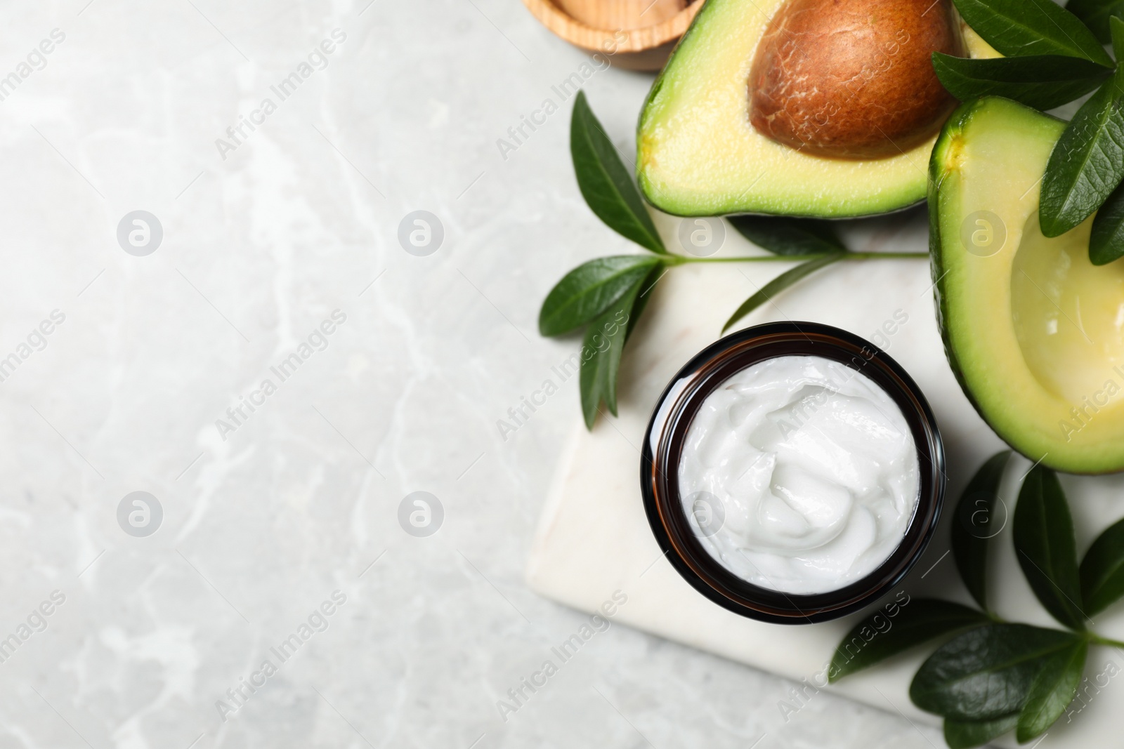 Photo of Jar of face cream and avocado on marble table, flat lay. Space for text
