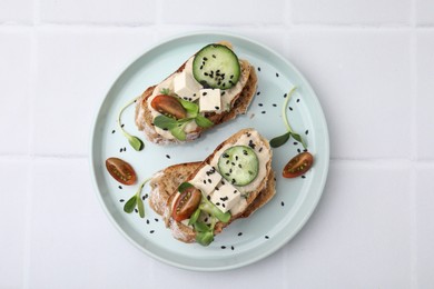 Tasty vegan sandwiches with tofu, cucumber, tomato and sesame seeds on white tiled table, top view