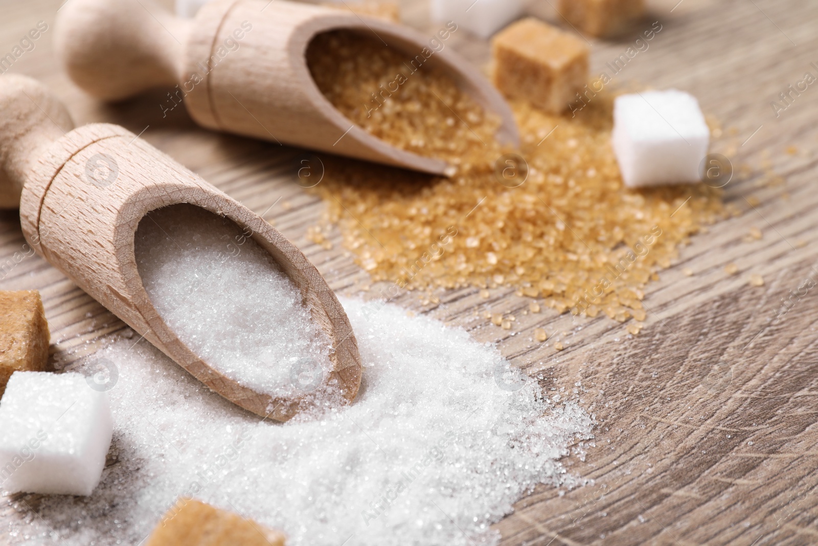 Photo of Scoops with different types of sugar on wooden table, closeup