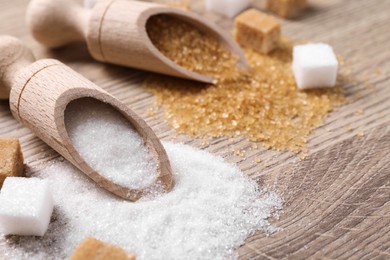 Scoops with different types of sugar on wooden table, closeup