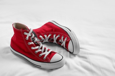 Pair of new stylish red sneakers on white fabric. Space for text