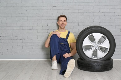 Photo of Male mechanic with car tires on brick wall background