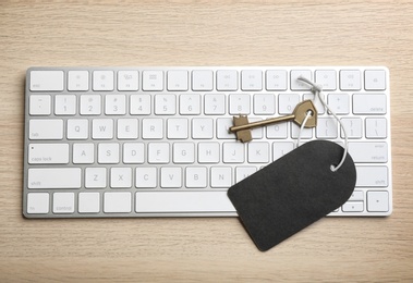 Key with blank tag and computer keyboard on wooden table, top view. Keyword concept