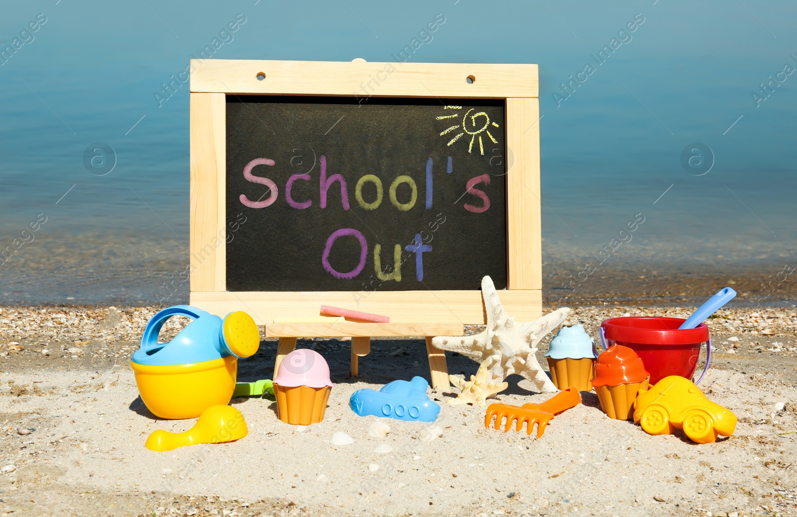 Image of Chalkboard with text SCHOOL'S OUT and toys on beach