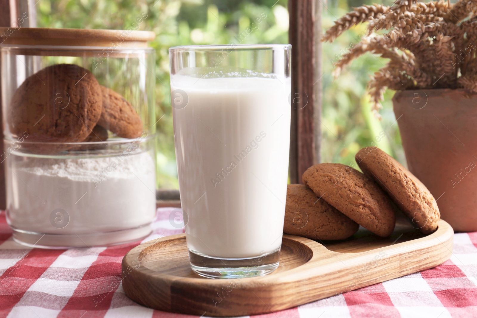 Photo of Glass of milk with cookies on red checkered tablecloth indoors